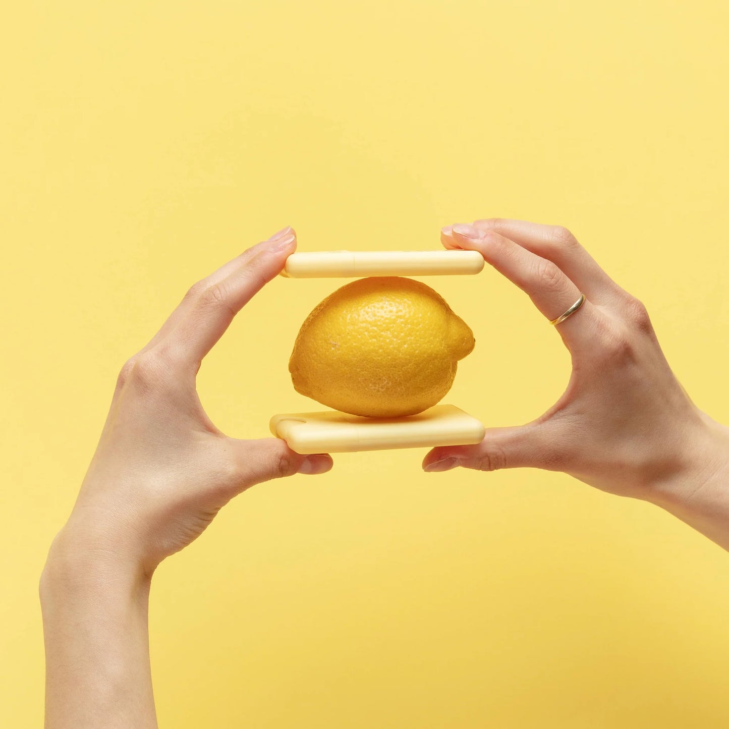 Fresh lemon balanced between two slim Noshinku Lemon pocket hand sanitizers against a bright yellow background, highlighting the compact refillable design and citrus-inspired scent.