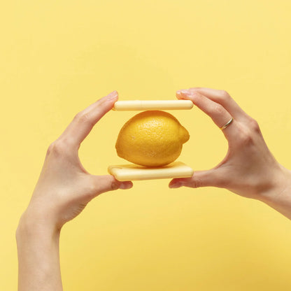 Fresh lemon balanced between two slim Noshinku Lemon pocket hand sanitizers against a bright yellow background, highlighting the compact refillable design and citrus-inspired scent.