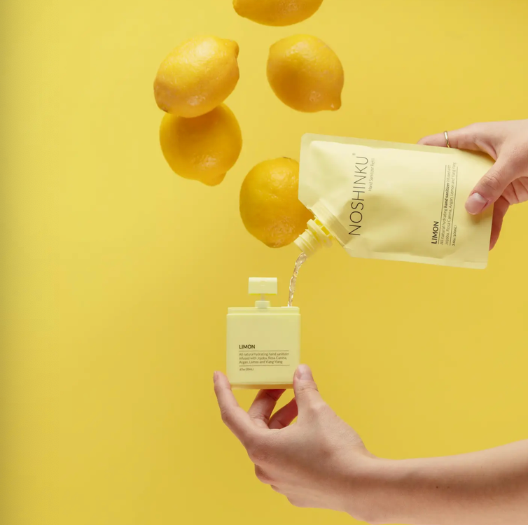 Noshinku Limon refill pouch pouring moisturizing hand sanitizer into a refillable pocket spray bottle beside fresh lemons.