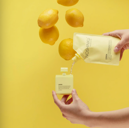 Noshinku Limon refill pouch pouring moisturizing hand sanitizer into a refillable pocket spray bottle beside fresh lemons.