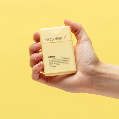 Hand holding Noshinku Limon refillable pocket hand sanitizer against a bright yellow background featuring refreshing lemon citrus scent notes and a sleek travel-friendly design. Exclusively at Area Boutique.