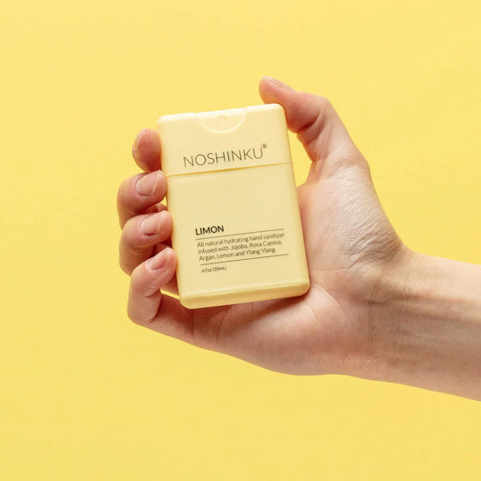 Hand holding Noshinku Limon refillable pocket hand sanitizer against a bright yellow background featuring refreshing lemon citrus scent notes and a sleek travel-friendly design. Exclusively at Area Boutique.
