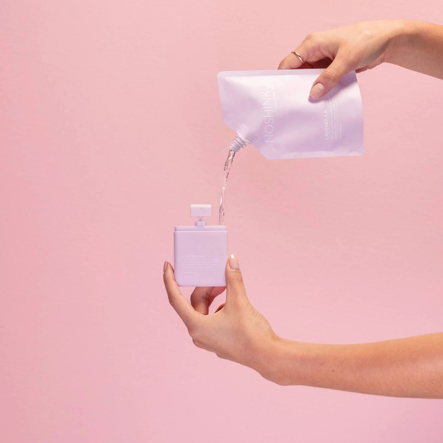 Refilling a Noshinku Lavendula pocket sanitizer using the Lavendula hand sanitizer refill pouch against a soft pink background.